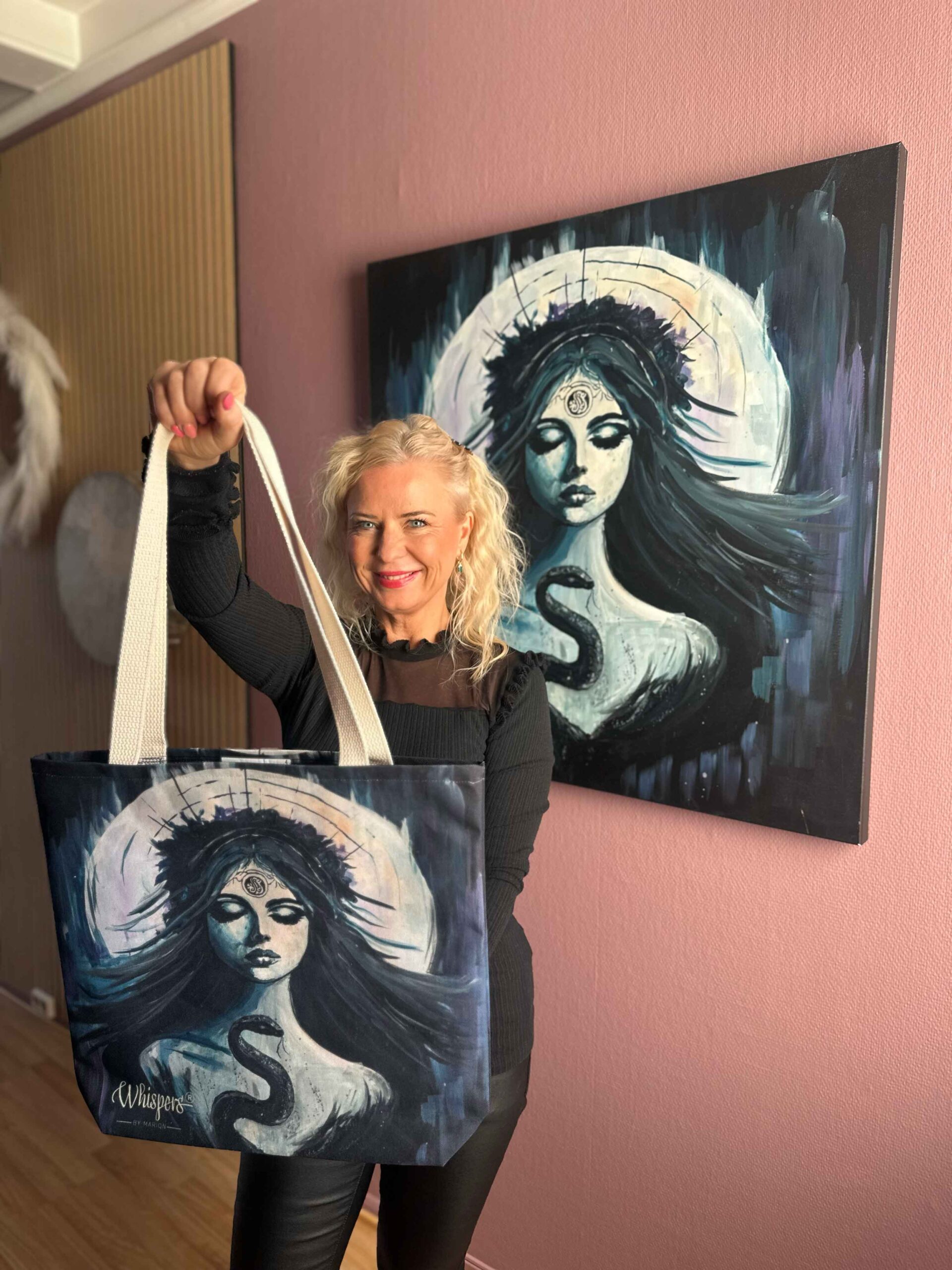 Kvinne holder tote bag med kunstmotiv fra Lilith’s Liberation foran originalmaleri, symbol på styrke og transformasjon